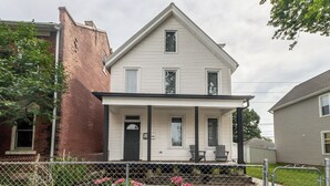 A two-story house with a front porch, a brick wall on the left, and a fenced garden with flowers. - Jackson Street Suites #1 (Dubuque)