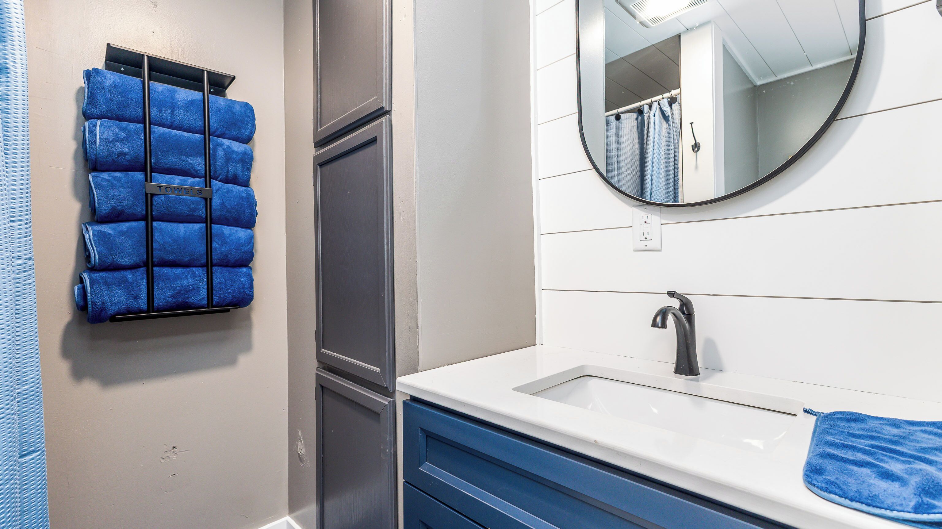 A bathroom with a white sink, a mirror, and a towel rack with blue towels.