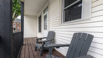 A wooden deck with two Adirondack chairs and a white house with windows.