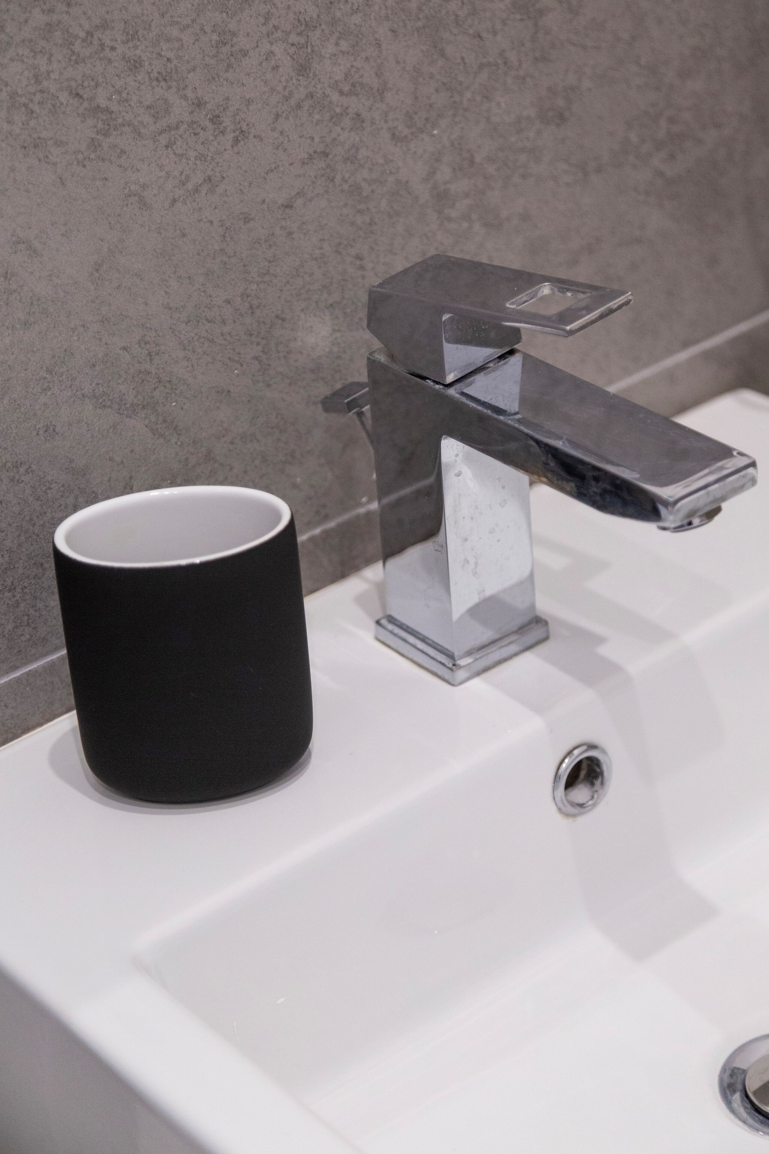 A bathroom sink with a black mug on the left and a chrome faucet.