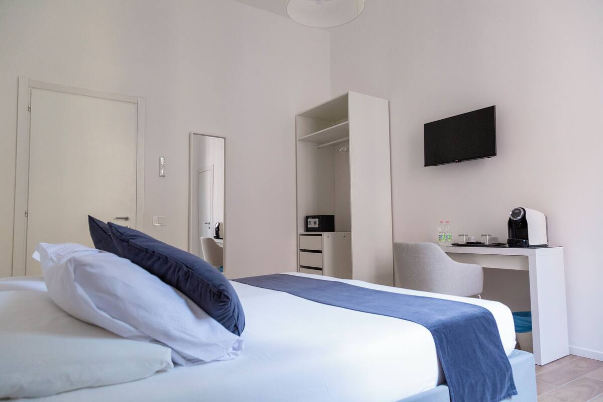 A hotel room with a bed, a desk, a chair, a television, and a wardrobe.