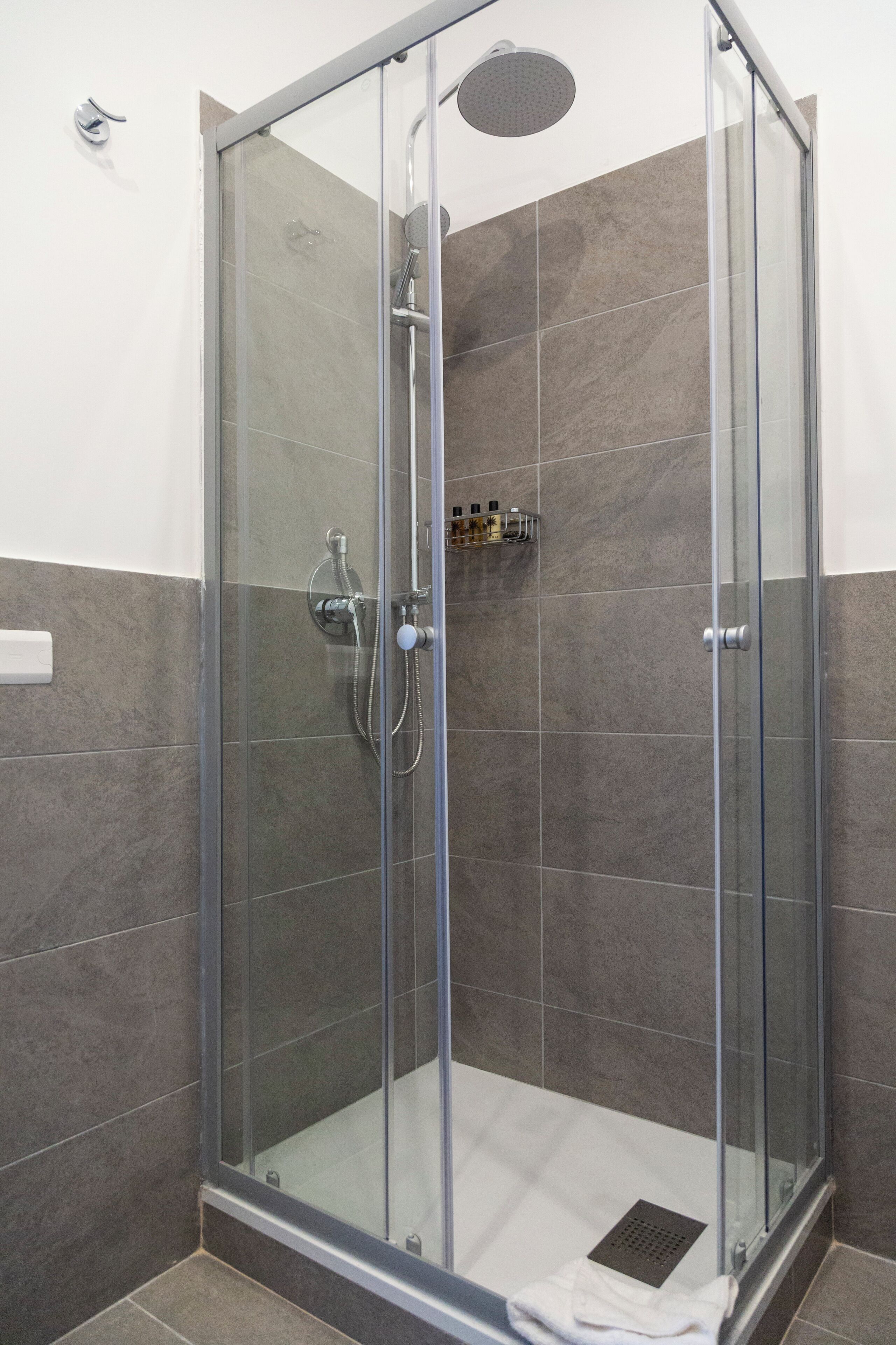 Una cabina de ducha con paredes de vidrio, cabezal de ducha de mano y grifo en la pared.