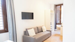 A modern room with a grey sofa, a flat-screen TV mounted on the wall, a wooden floor, and a sliding door leading to a balcony. - Relais Borsieri (Rome)