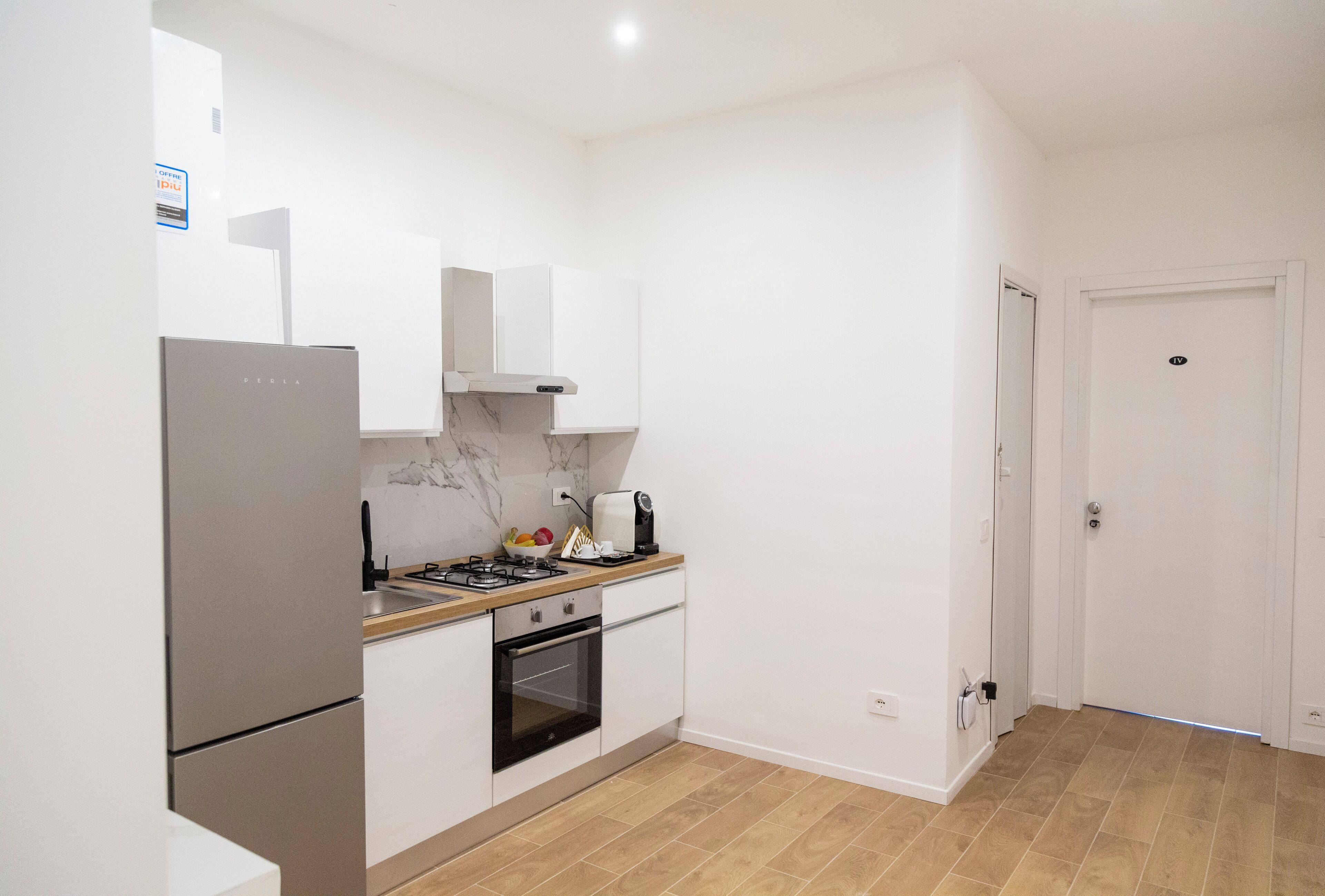 A compact kitchen with a refrigerator, stove, oven, and white cabinets.