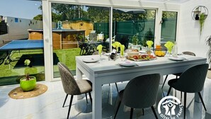 A modern outdoor dining area with a glass table, chairs, and a ping pong table.