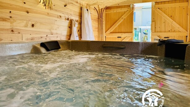 A wooden spa with a hot tub, wooden walls, and a view of the outside.