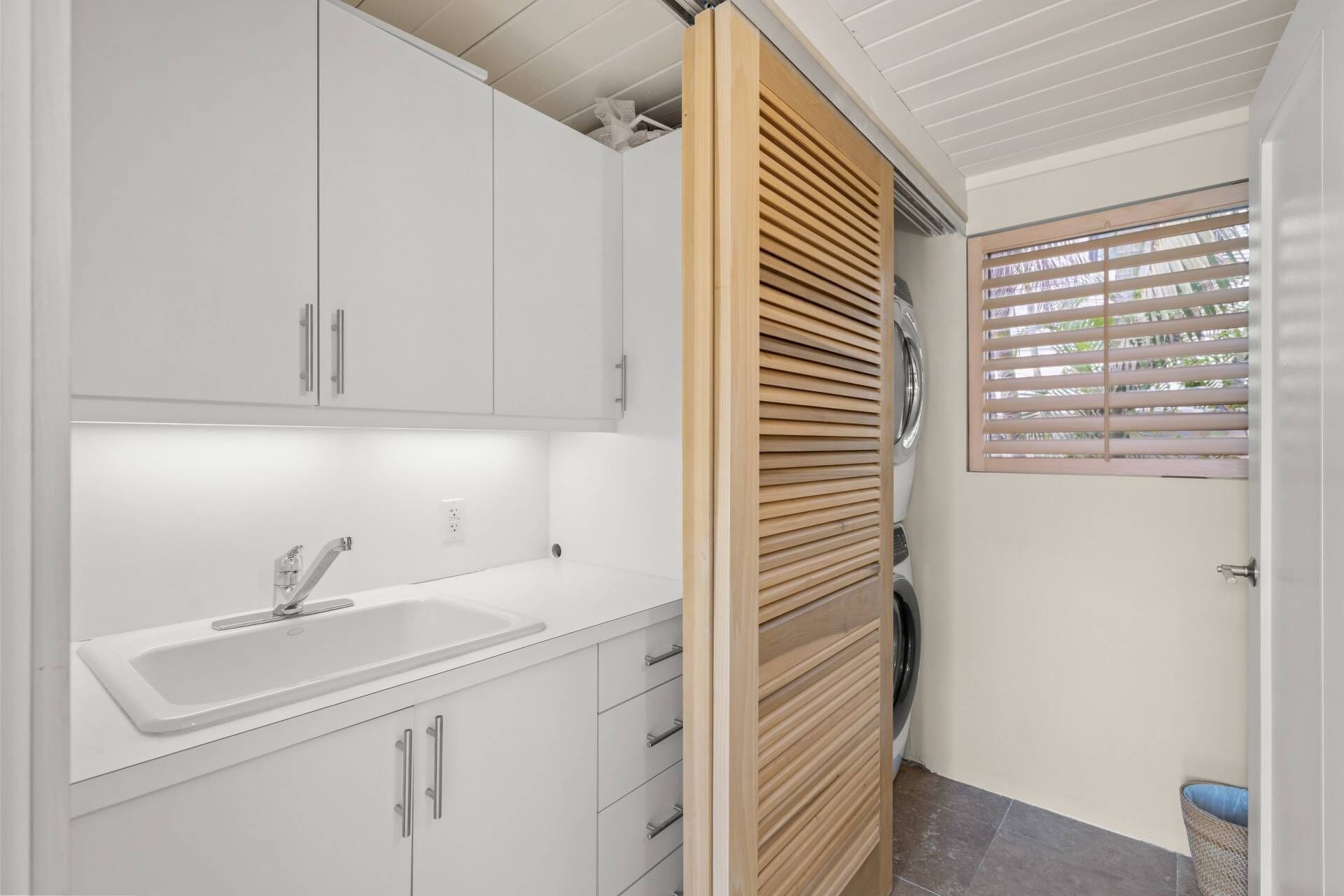 A modern bathroom with a white sink, cabinets, and a wooden slatted door.