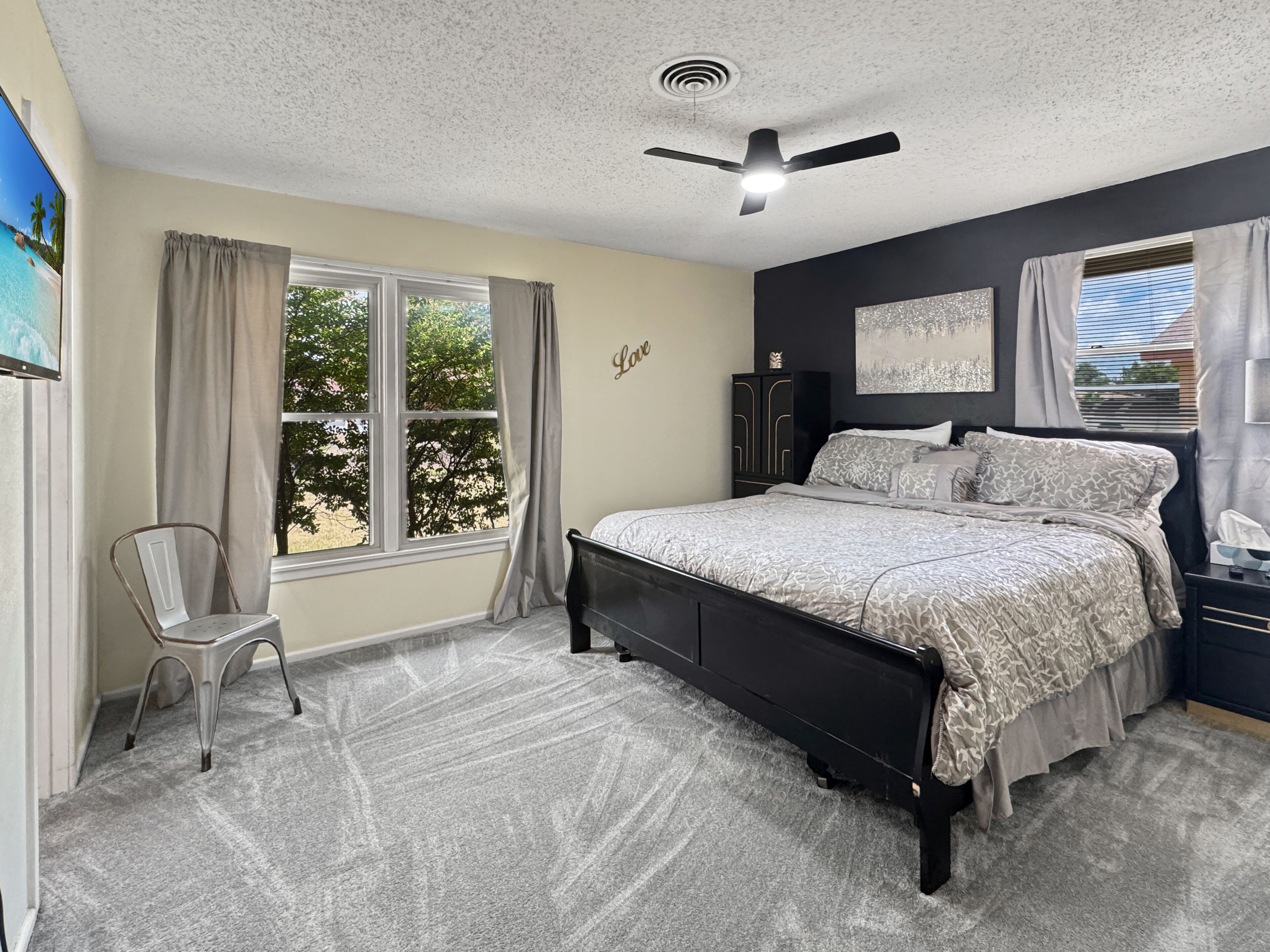 A bedroom with a bed, a chair, a ceiling fan, and a window with curtains.