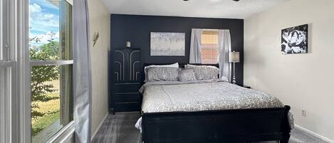 Un dormitorio con cama, ventilador de techo, ventana con cortinas y obras de arte en las paredes.
