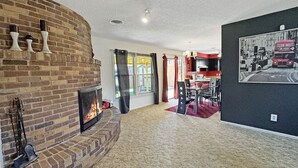 Ein Wohnzimmer mit Kamin aus Ziegelsteinen, einem Essbereich mit rotem Teppich und einer schwarzen Wand mit Stadtbildgemälde.
