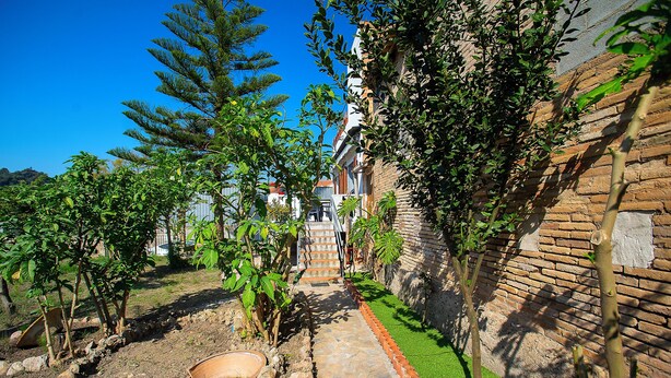 Un sendero estrecho que lleva a un edificio con pared de ladrillo y un pequeño jardín con césped y árboles.