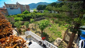 Una terraza con baranda blanca, una mesa y sillas, con vista a un jardín con árboles y un edificio al fondo.
