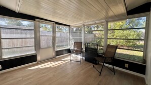A covered patio with wooden flooring, two chairs, and large windows overlooking a backyard. - Sunny 2BR Retreat · Enclosed Patio · Pet Friendly · Near Gulf Beaches (Port Richey)