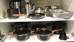 Un estante de cocina con diferentes utensilios, incluyendo ollas, sartenes, un hervidor y una sartén.