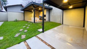 Un patio techado al aire libre con zona de estar, un sendero de hormigón y césped.