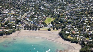 An aerial view of a coastal residential area with houses, a beach, and clear turquoise waters.