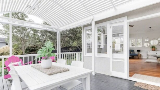 A covered outdoor area with a white table and chairs, a potted plant, and a wooden deck.