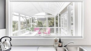 A modern kitchen with a large window overlooking a balcony with pink chairs and a white railing.