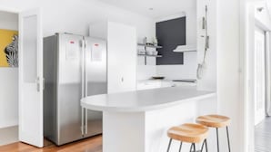 A modern kitchen with white cabinetry, a central island with stools, and stainless steel appliances.