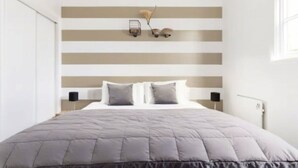 A bedroom with a bed, a striped wall, and a nightstand with a lamp.