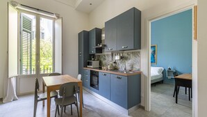 Une cuisine compacte dotée d’appareils électroménagers modernes, un coin repas avec une table et des chaises, et une chambre à coucher avec un lit et une table de chevet.