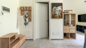 Un intérieur moderne avec un banc en bois, un porte-manteau, une porte, un tableau et un téléviseur posé sur un meuble.