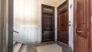 Un couloir avec une porte noire, une porte blanche et un paillasson.