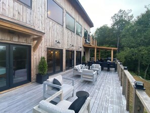 Eine Holzterrasse mit Sitzgelegenheiten im Freien, großen Fenstern und einer Pergola.