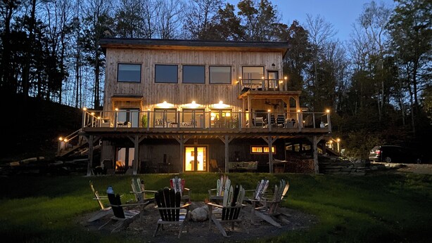 A two-story wooden cabin with a balcony, outdoor seating area, and a ski rack. - Stunning views, Luxurious, Peaceful, dog friendly, king beds,fire pit,WIFI,AC,EV (Townshend)