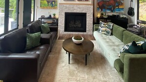 A living room with a fireplace, four bear paintings, a green sofa, a brown leather couch, and a coffee table. - Stunning views, Luxurious, Peaceful, dog friendly, king beds,fire pit,WIFI,AC,EV (Townshend)