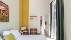 A bedroom with a bed, a chair, a wooden shelf, and a painting on the wall.