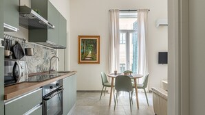 A compact kitchen with modern appliances, a dining area with a table and chairs, and a view through a window with curtains.