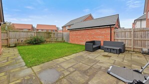 Une terrasse à l’arrière de la maison, avec un sol en pierre, une petite pelouse et un mur en briques.