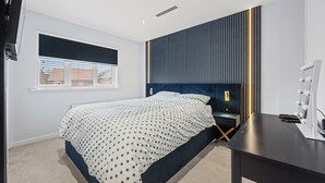Une chambre à coucher moderne avec un lit, des tables de chevet et un bureau agrémenté d’un miroir et de lampes.