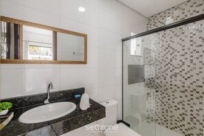 Ein modernes Badezimmer mit einem weißen Waschbecken, einem großen Spiegel und einer Dusche mit einer Wand aus gemusterten Fliesen.