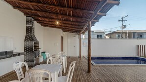 A covered patio area with a brick fireplace, outdoor seating, and a swimming pool.