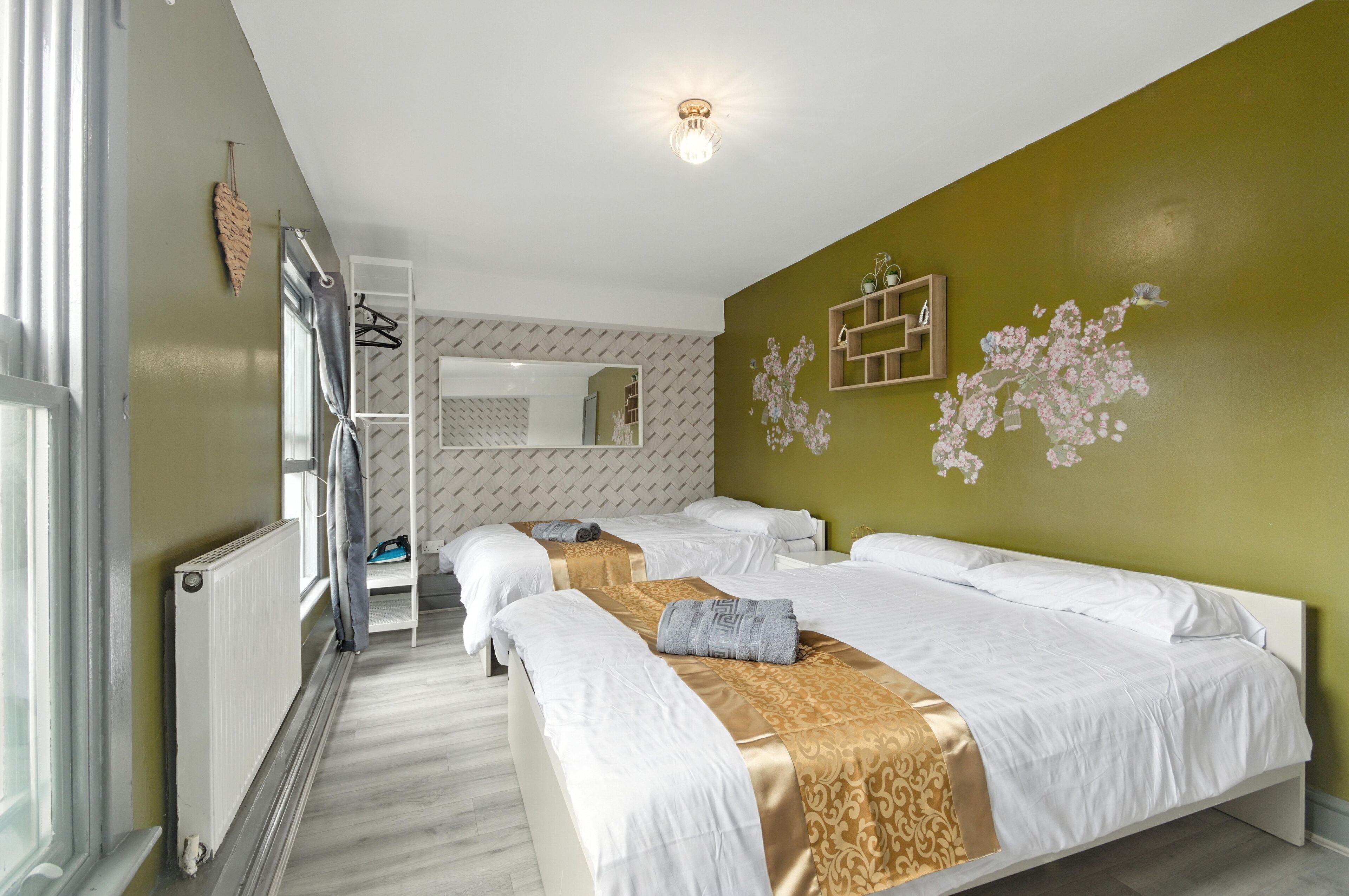 A hotel room with a bed, a small table, a mirror, and a wall-mounted light fixture.
