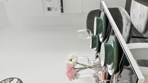A modern kitchen with a white countertop, a built-in stove, and a dining area with a chair and a table.