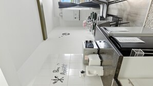 A modern kitchen with a white countertop, a coffee machine, a fire extinguisher, and a window with a view of buildings.