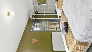 A compact hotel room with a bed, a small desk, a mirror, and a window with a view of buildings.