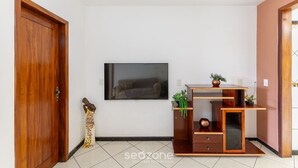 Een kamer met een houten deur, een flatscreen televisie aan de muur en een houten dressoir met planken, plus een klein beeldje op de vloer.