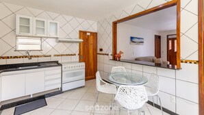 Een kleine keuken met witte kastjes, een fornuis en een glazen eettafel met witte stoelen.