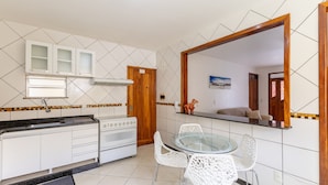 Een kleine keuken met witte kastjes, een fornuis en een glazen eettafel met witte stoelen.