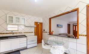 Een kleine keuken met witte kastjes, een fornuis en een glazen eettafel met witte stoelen.