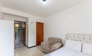 Een slaapkamer met een bed, een bank, een houten deur en een betegelde vloer.