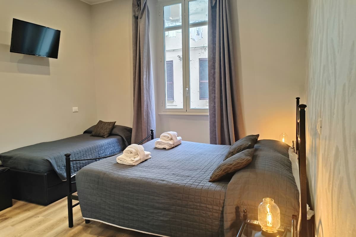 A bedroom with two beds, a TV mounted on the wall, and a window with curtains.