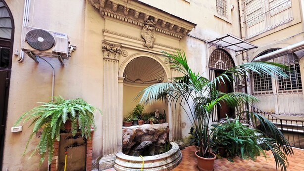 A courtyard with a fountain, potted plants, and a tiled floor. - Nicole Suite (Rome)