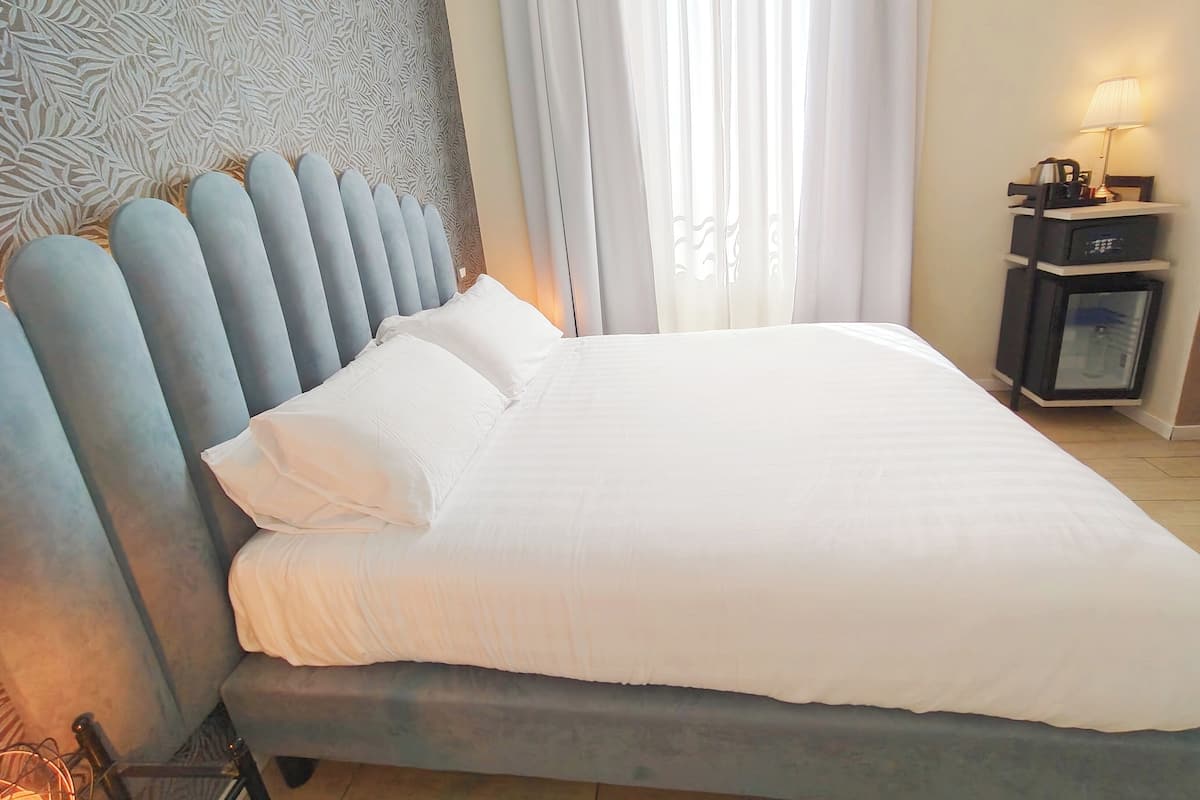 A neatly made bed with white linens, a patterned headboard, and a bedside table with a lamp.