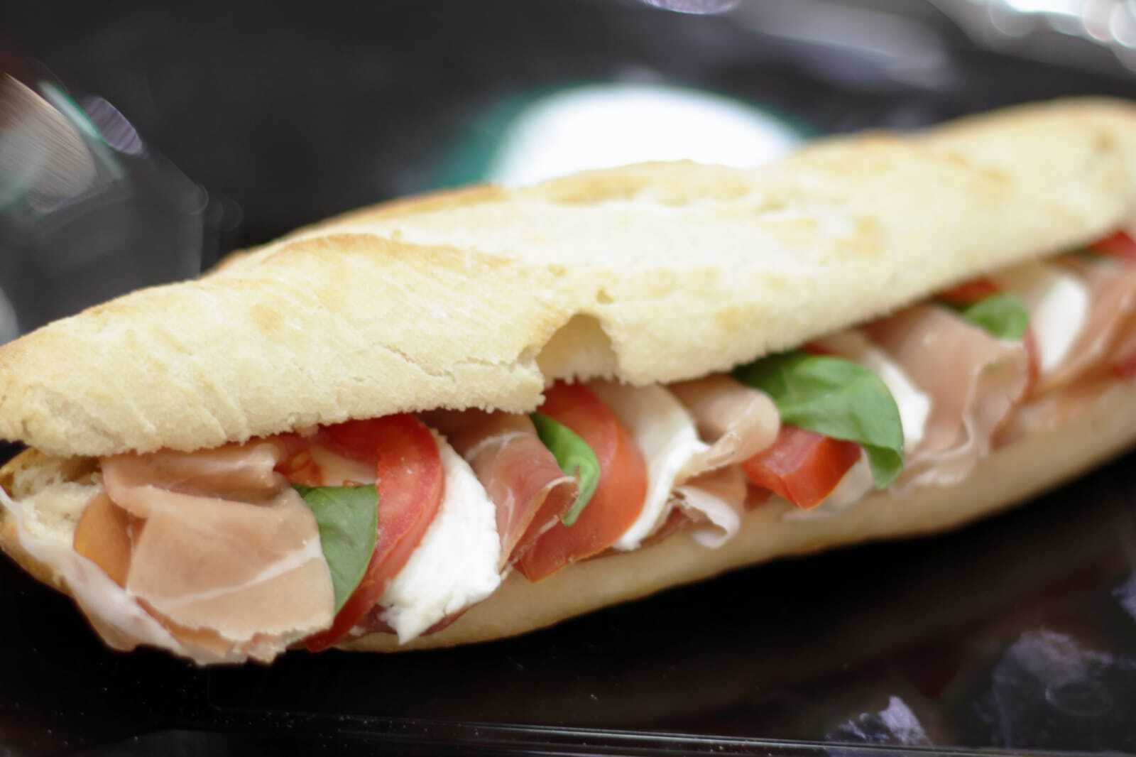 Un sándwich con un panecillo crujiente, relleno de carnes en rodajas, tomates y hojas verdes.