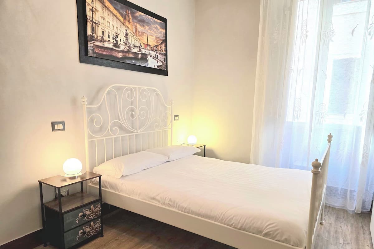 A neatly made bed with a white headboard, two bedside tables with lamps, a wooden floor, and a framed picture on the wall.